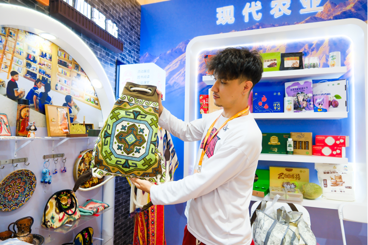 現(xiàn)場維吾爾族小伙向人們展示哈薩克族勾繡技藝。新疆哈薩克族鏈條袖勾繡是一種結合機器繡與手工勾秀的獨特工藝。如今，不僅保留了傳統(tǒng)圖案，還融入現(xiàn)代設計元素。目前，其所在村子約140名工人負責這一非物質文化遺產項目的傳承與發(fā)展，主要在農閑時進行勾繡。有些村民年收入可達25000至30000元人民幣。不僅促進了當?shù)亟洕l(fā)展，也保障了傳統(tǒng)文化的延續(xù)。